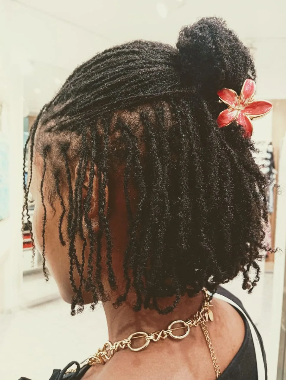 Micro locs in a half-up bun with a red flower clip, side view